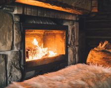 A dark living room features a lit wood-burning fireplace in the center of the wall. 